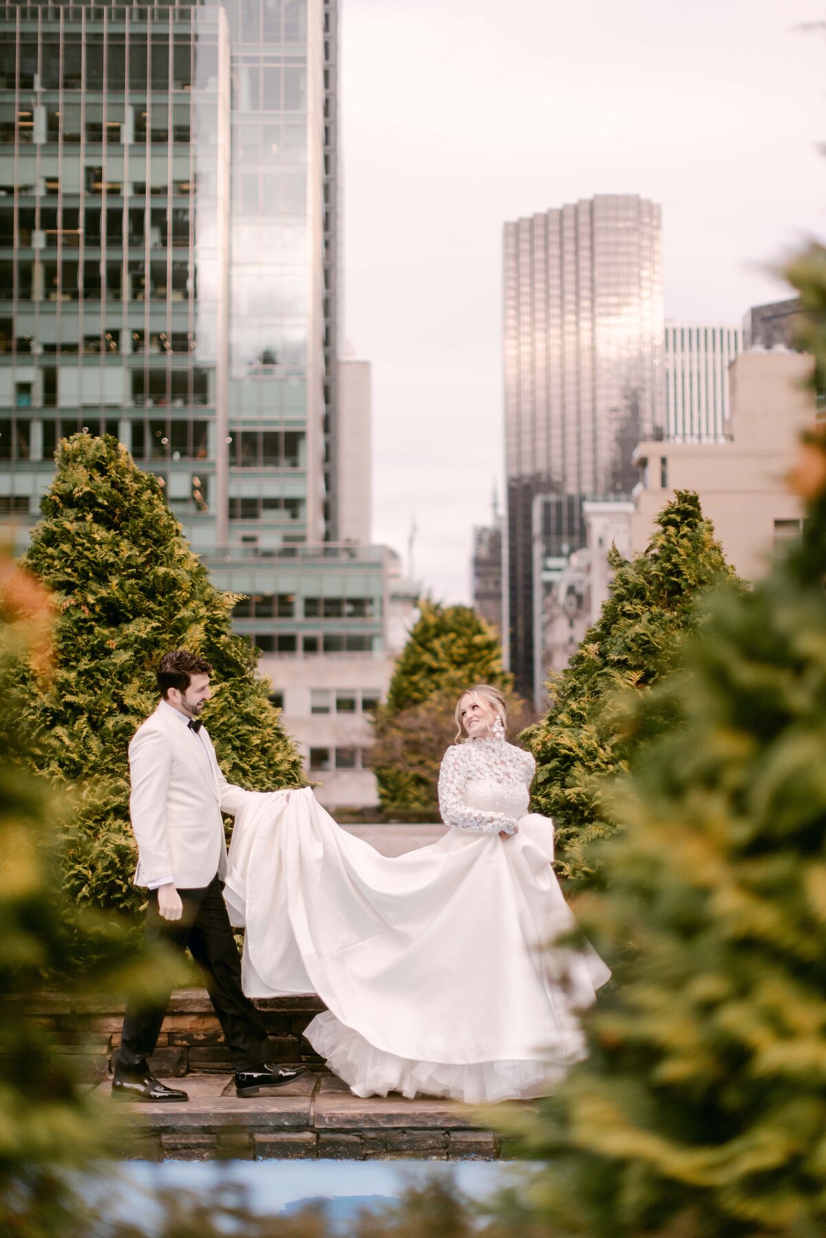 Groom holding a brides dress as they walk on a rooftop