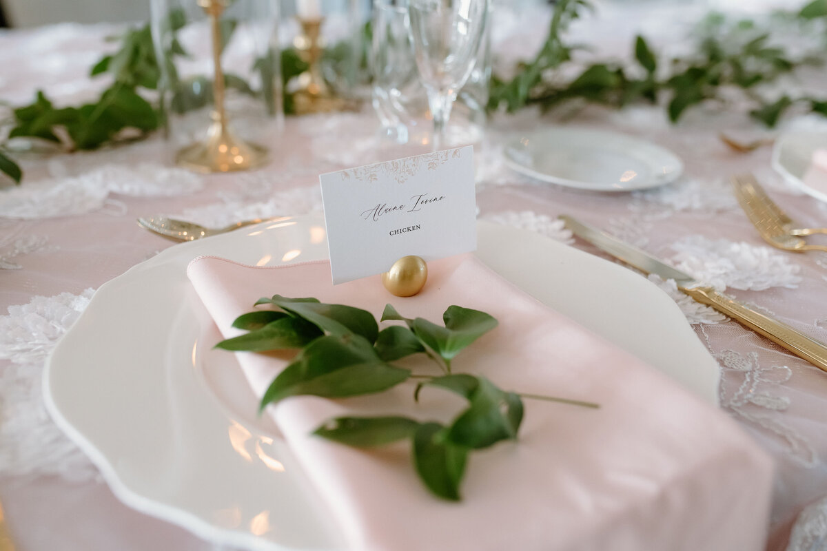 Elegant wedding place card on blush napkin with greenery, part of luxury wedding day stationery suite.