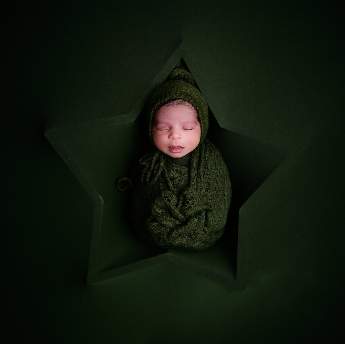 Beth Benecki of E. Benecki Photography captures this  newborn placed sleeping in a star covered by dark green fabric during his newborn photo session..