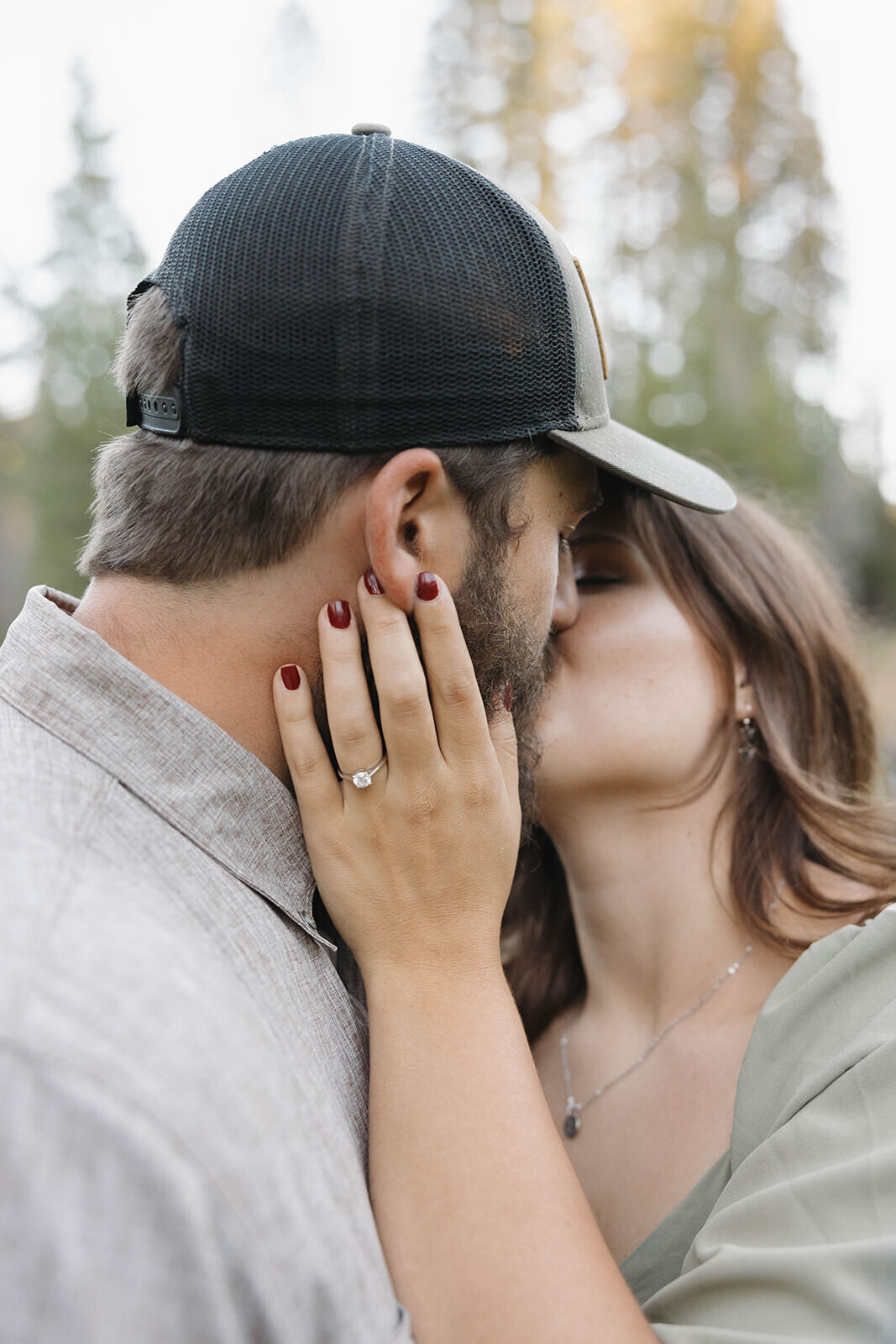 Engaged couple kissing in a pine meadow, ring in view