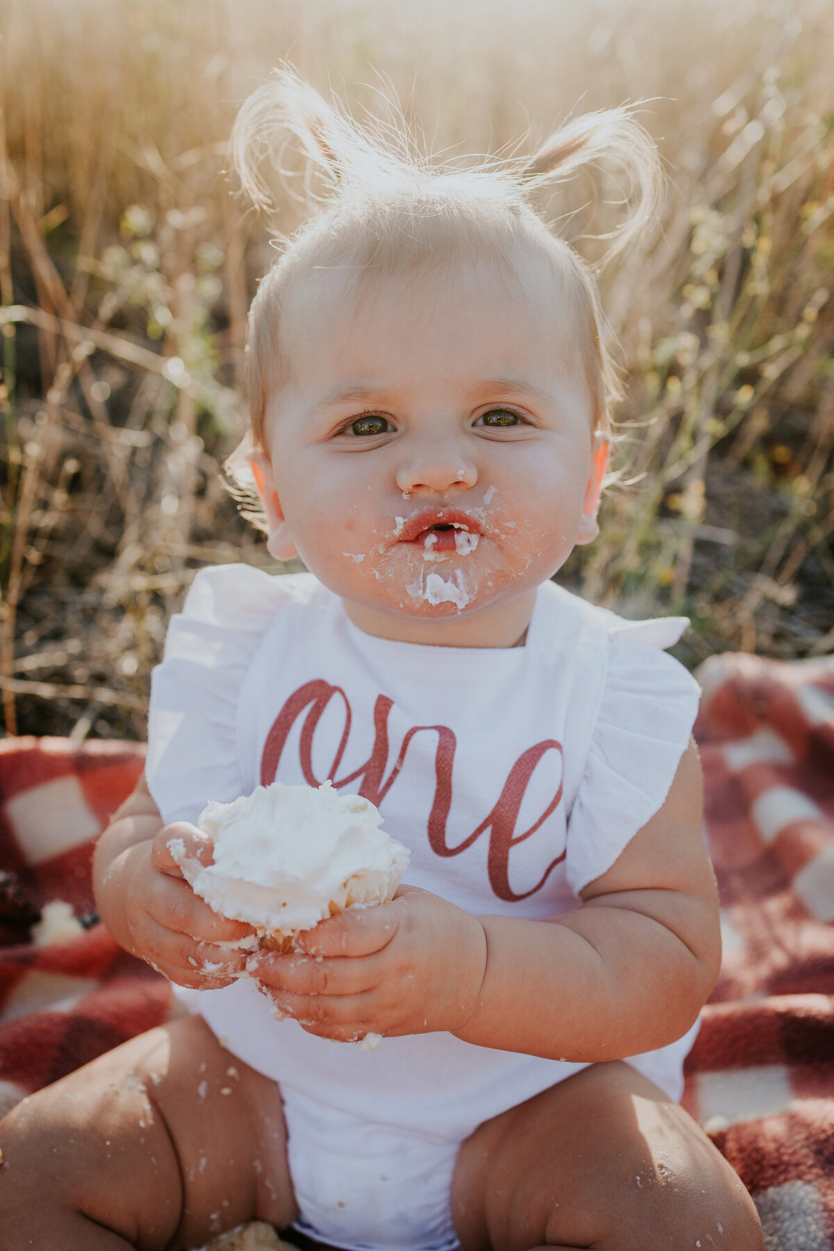 One year old girl gives camera a puzzled look as she hold a frosted cupcake.