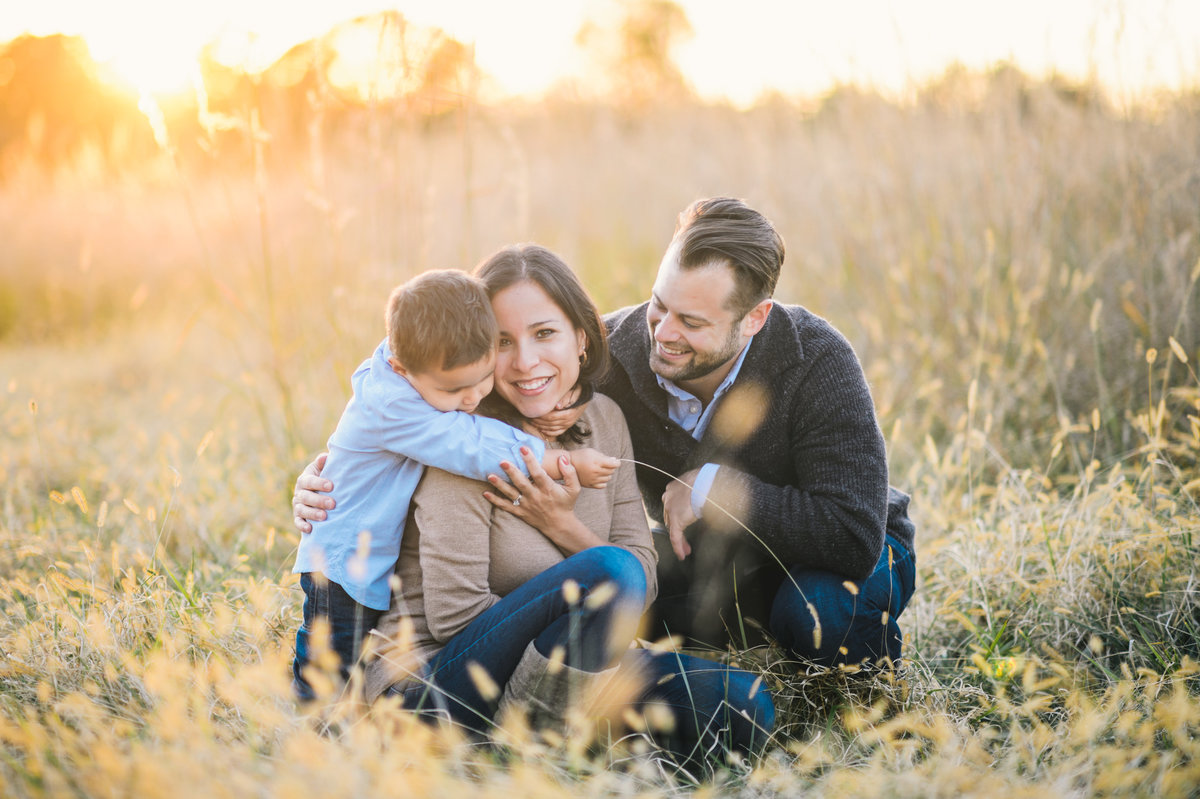 Family embracing in a field with tall grass.
