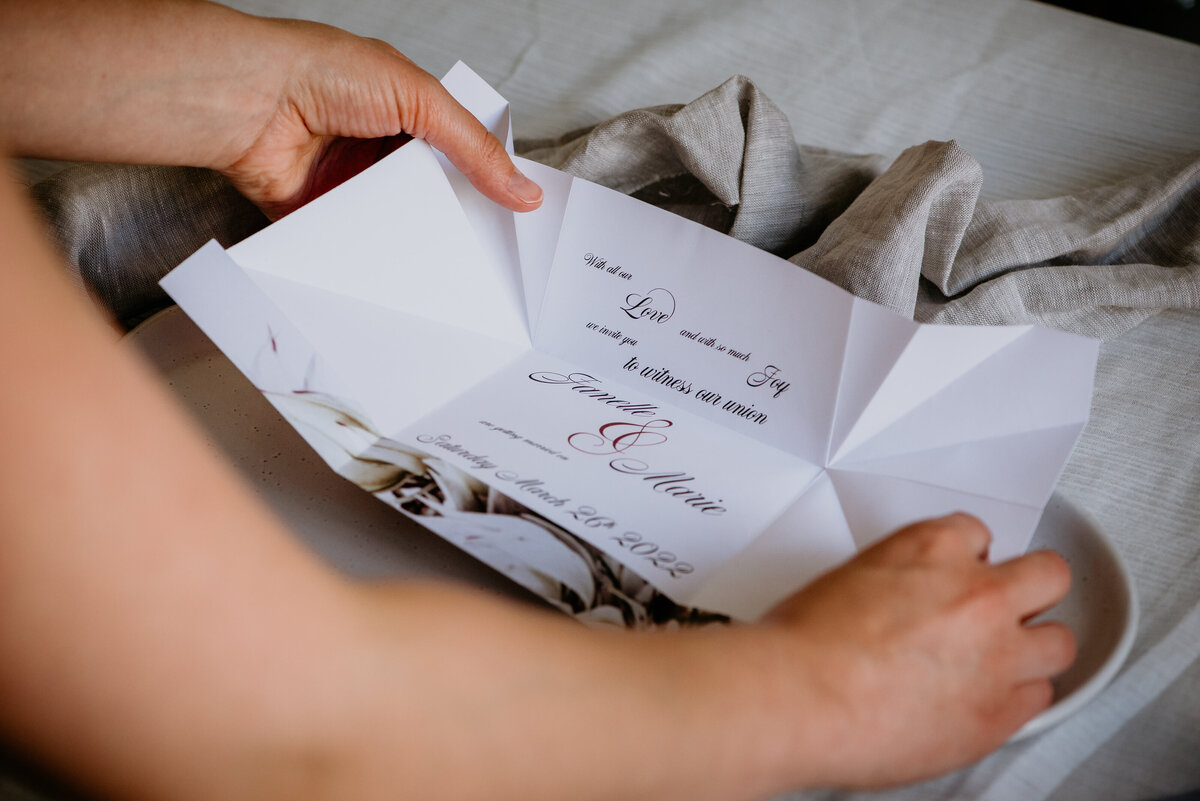 Hands unfolding an origami wedding invitation with elegant script font and ampersand