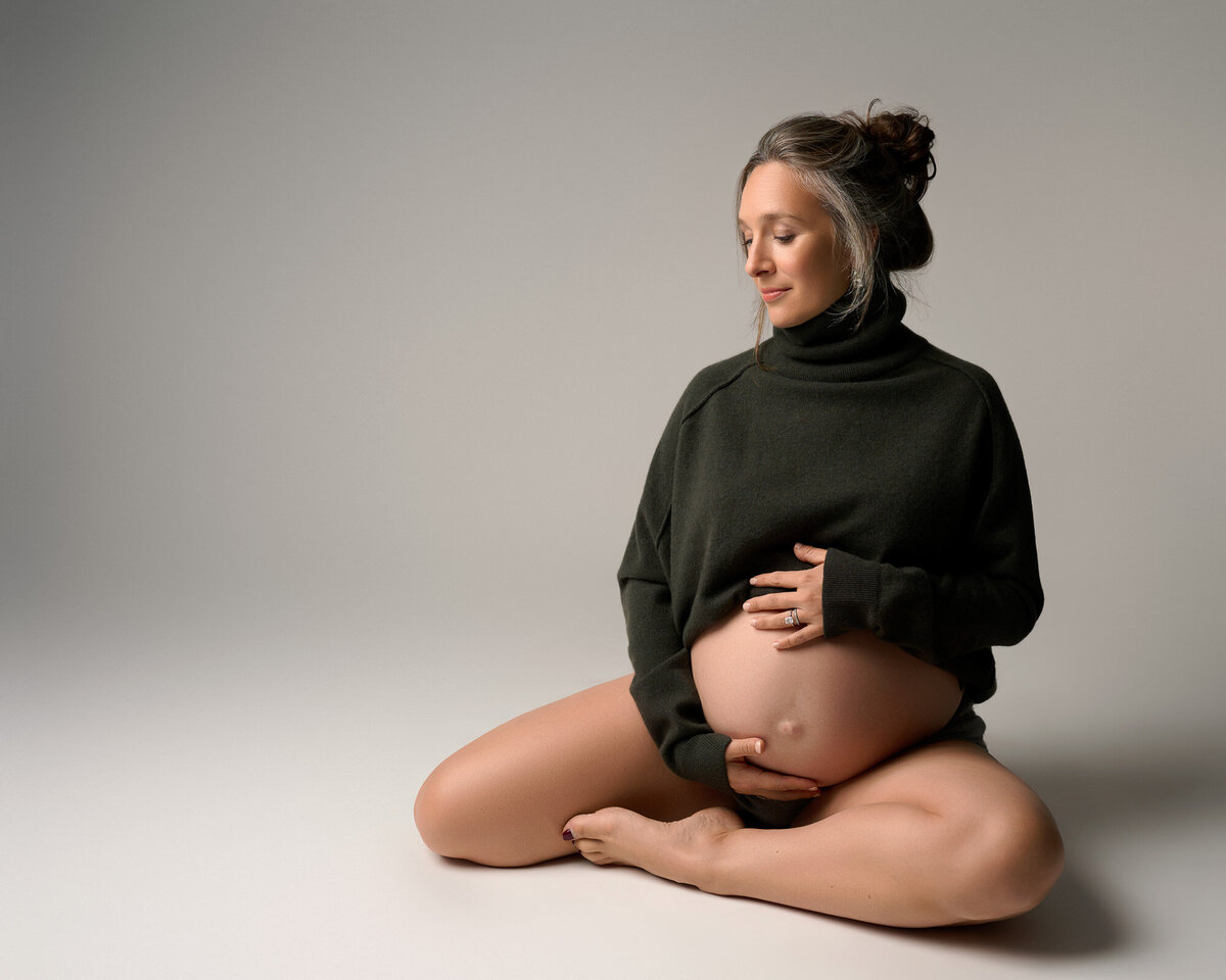 Expectant mother cradling baby bump in black fitted top during intimate studio maternity photoshoot