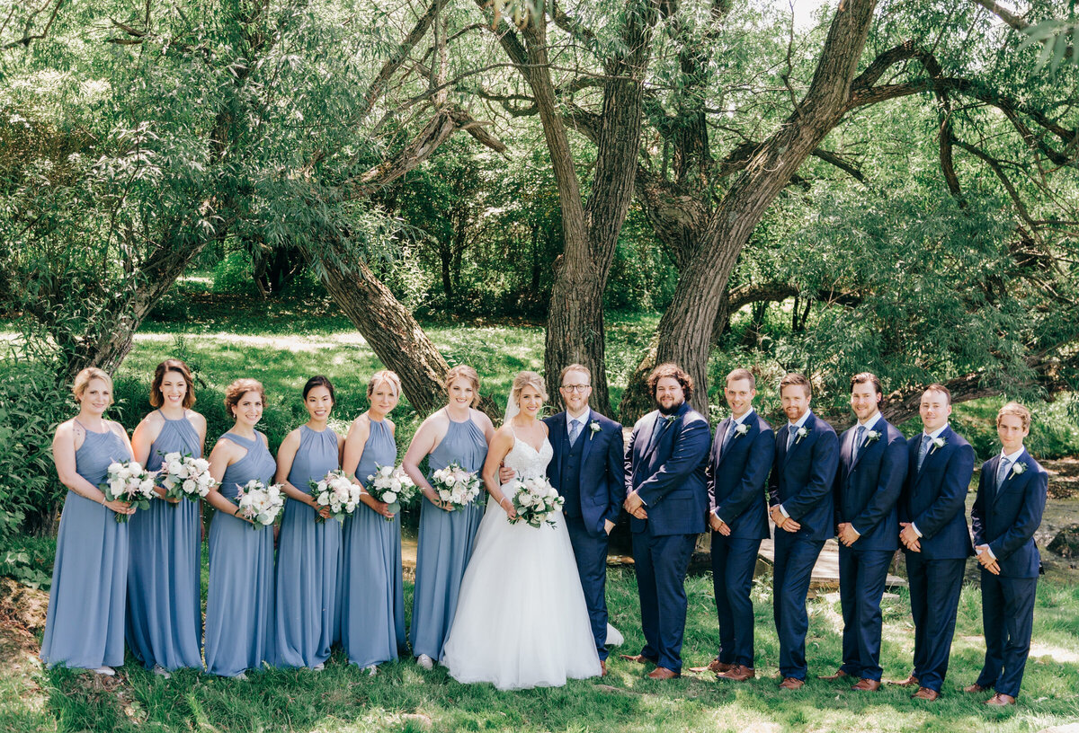 Elegant outdoor wedding party photo of bridesmaids in light blue and groomsmen in dark navy suits