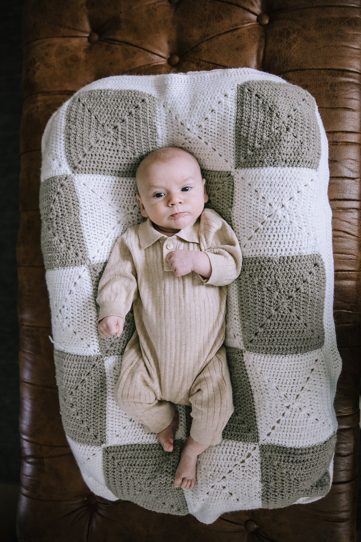 Baby boy cuddled under a checkered blanket.