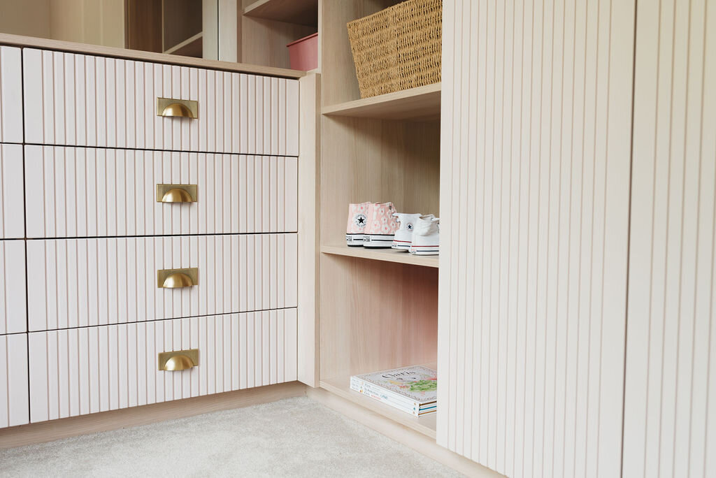 A close-up view of a modern pale pink dresser with gold half-moon handles. The dresser has a ribbed texture on the drawer fronts and features four drawers.