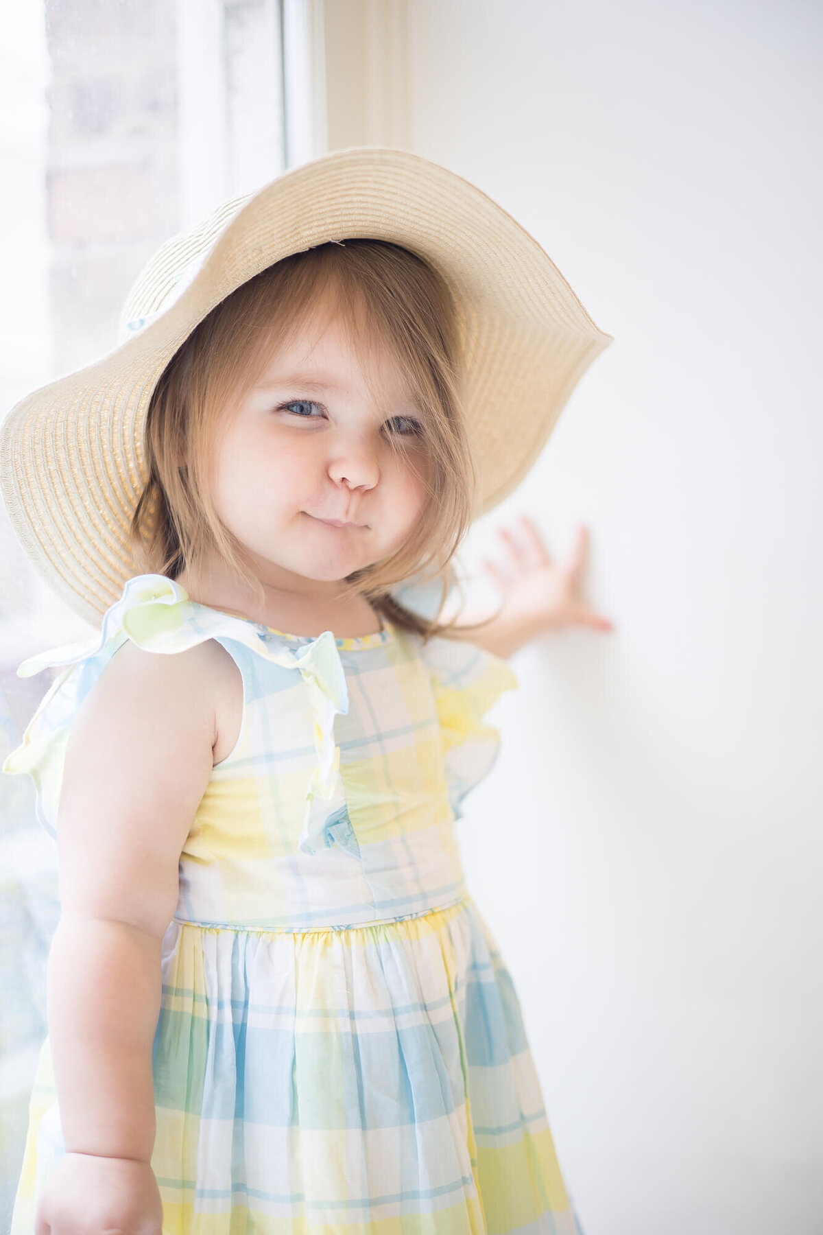 Toddler girl in a sunhat and sundress making a silly face