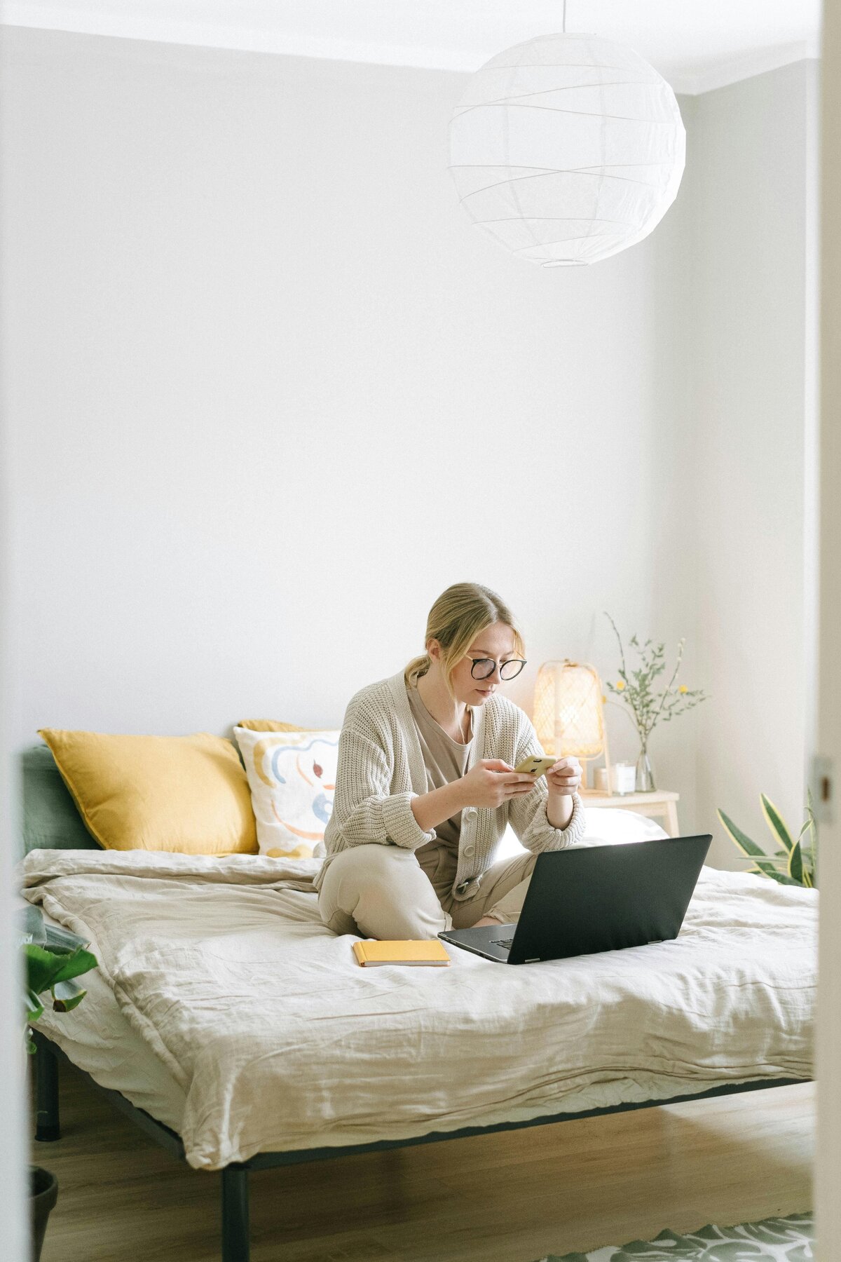 young girl sitting on bed on phone and computer