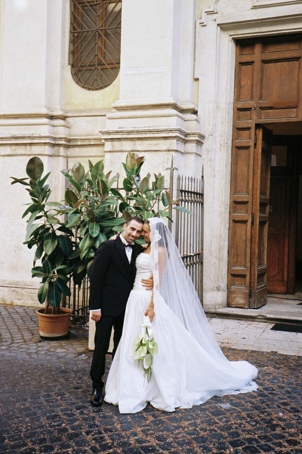 Bride and groom posing in front of Roman church door after ceremony

