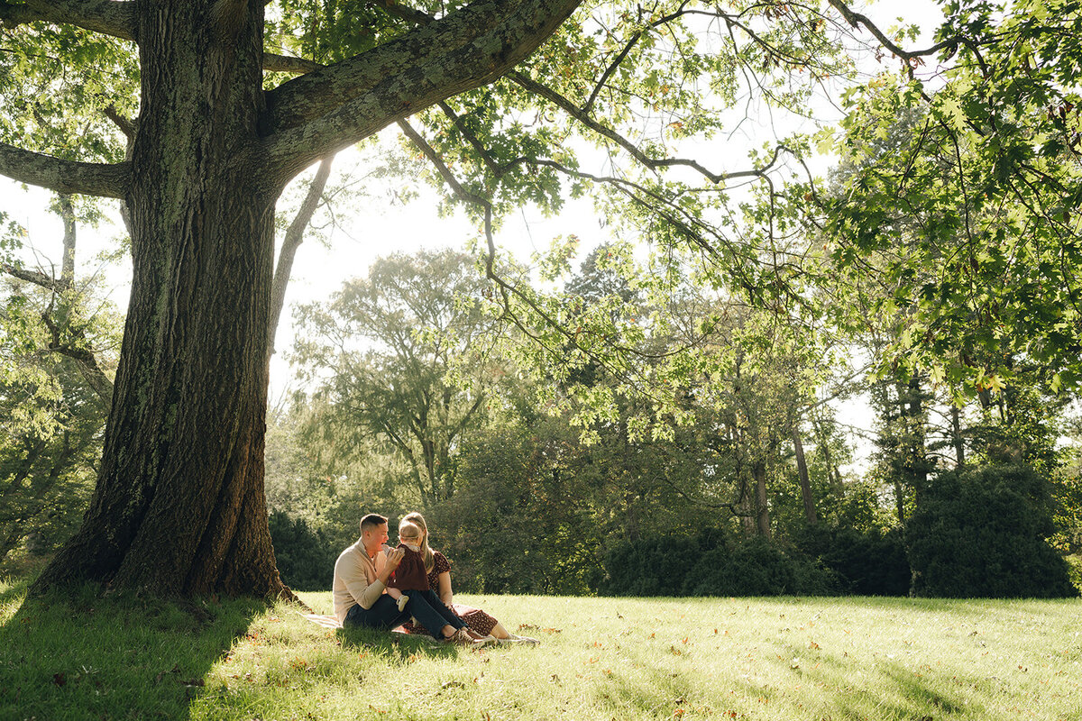 Family of three gathered under a large oak tree during a candid outdoor family photography session