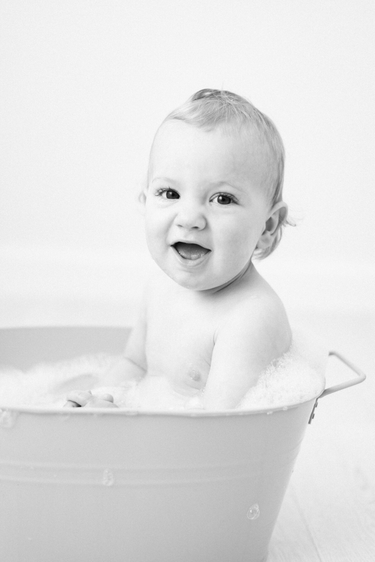 Baby boy in a bubble bath smiling during cake smash photoshoot in Billingshurst