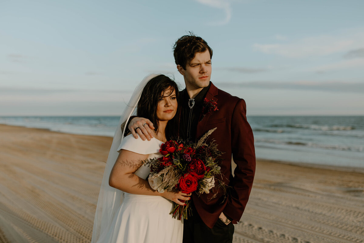couple standing close together on the east coast with the ocean behind them