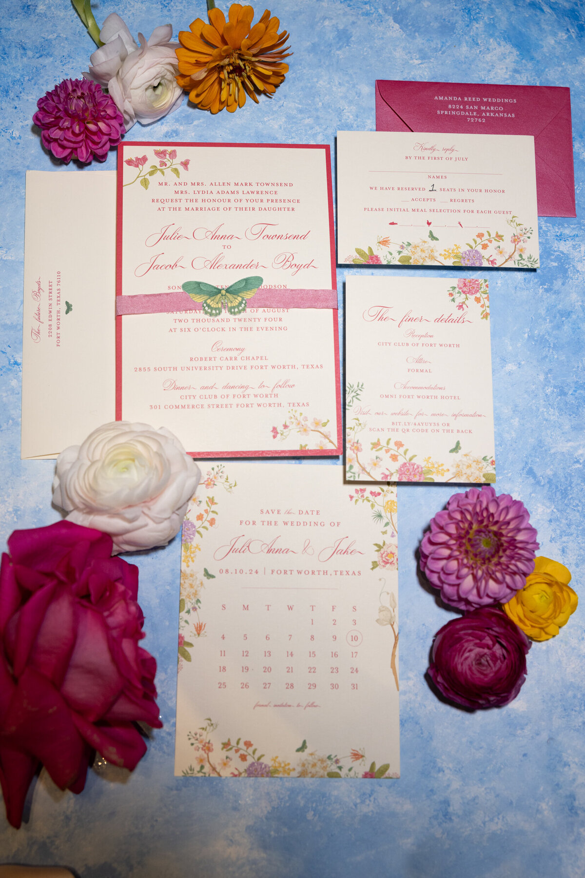 A wedding photo of the wedding invites laid on a linen backdrop with flowers surrounding the invitations
