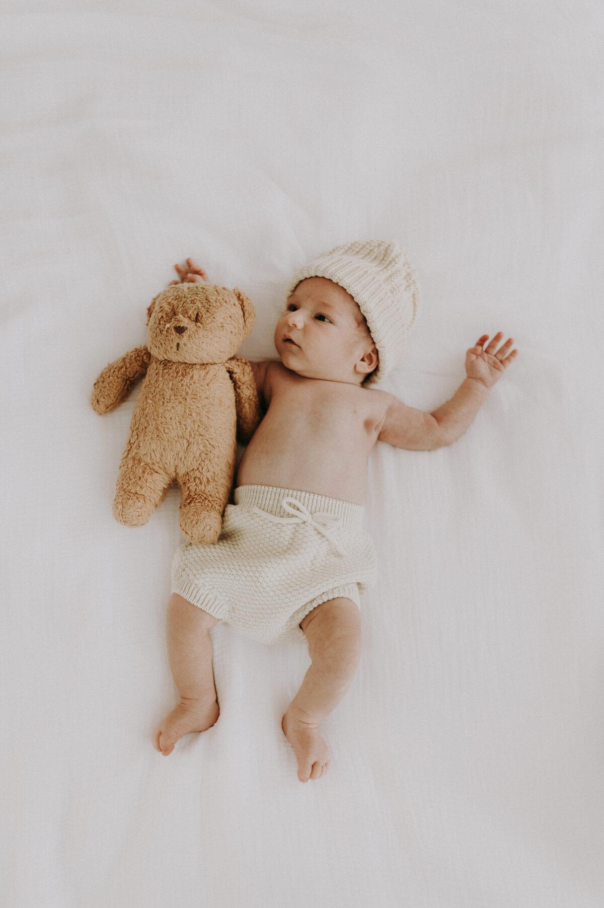Baby ligt op het bed met teddybeer.