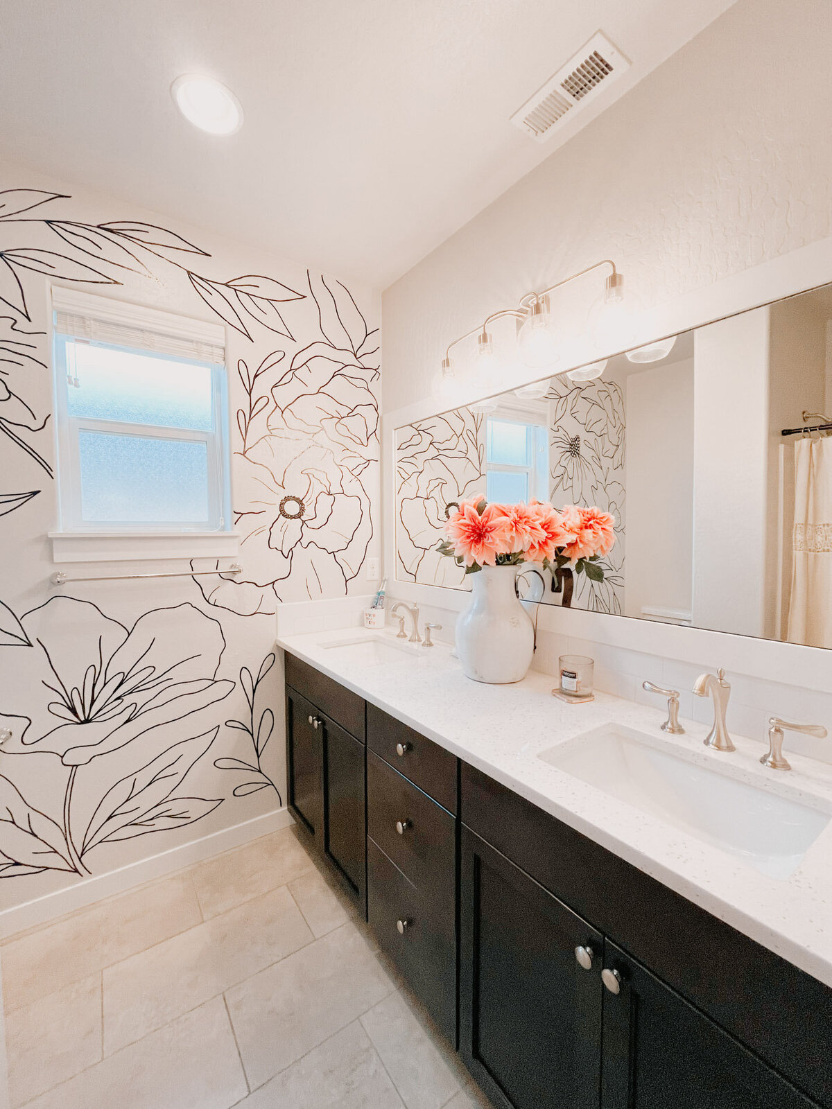 A guest bathroom with a sink featuring a back wall with a window and delicate custom florals painted on it and flowers in a vase on the counter representing full service design and calligraphy by Life in Letters.