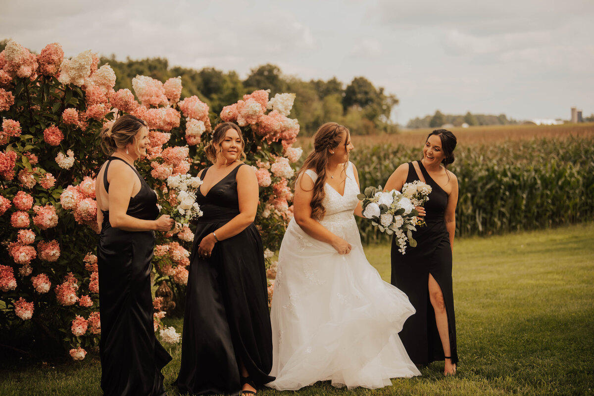 bride laughing with her bridesmaids in front of pink flowers