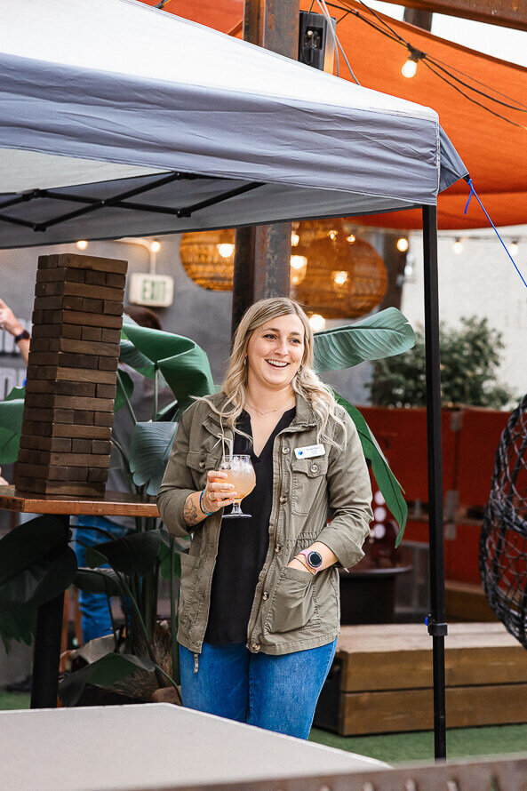 Girl in green jacket holds drink with jenga blocks behind her.