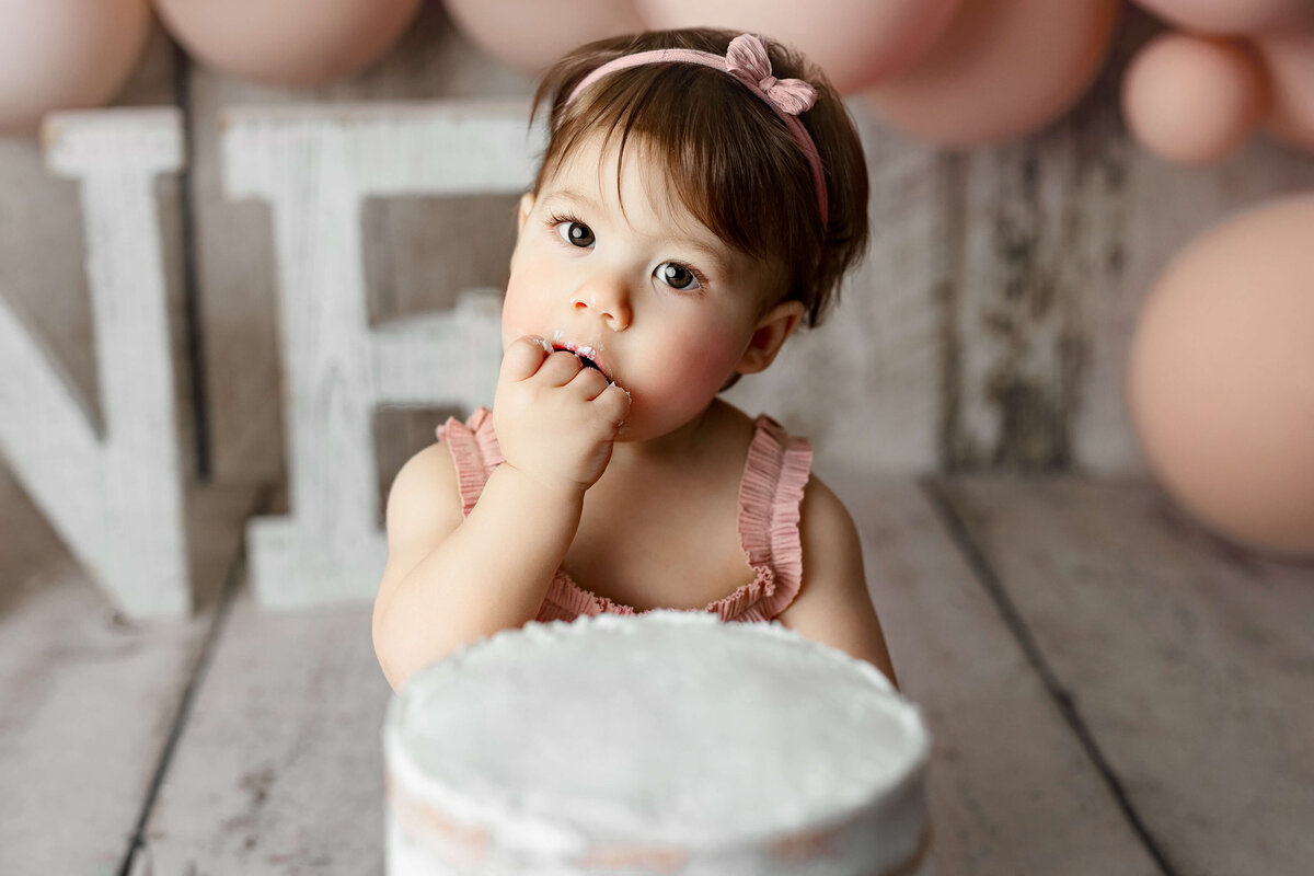 one year old girl eating her ibirthday cake at her one year old birthday session