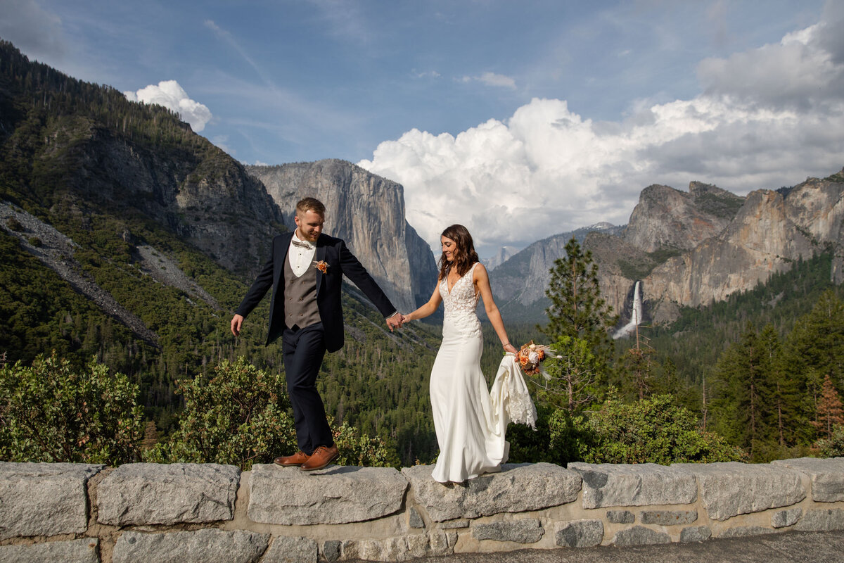 A bride and groom walk along a rock wall in Yosemite as their California elopement photographers take their pictures.