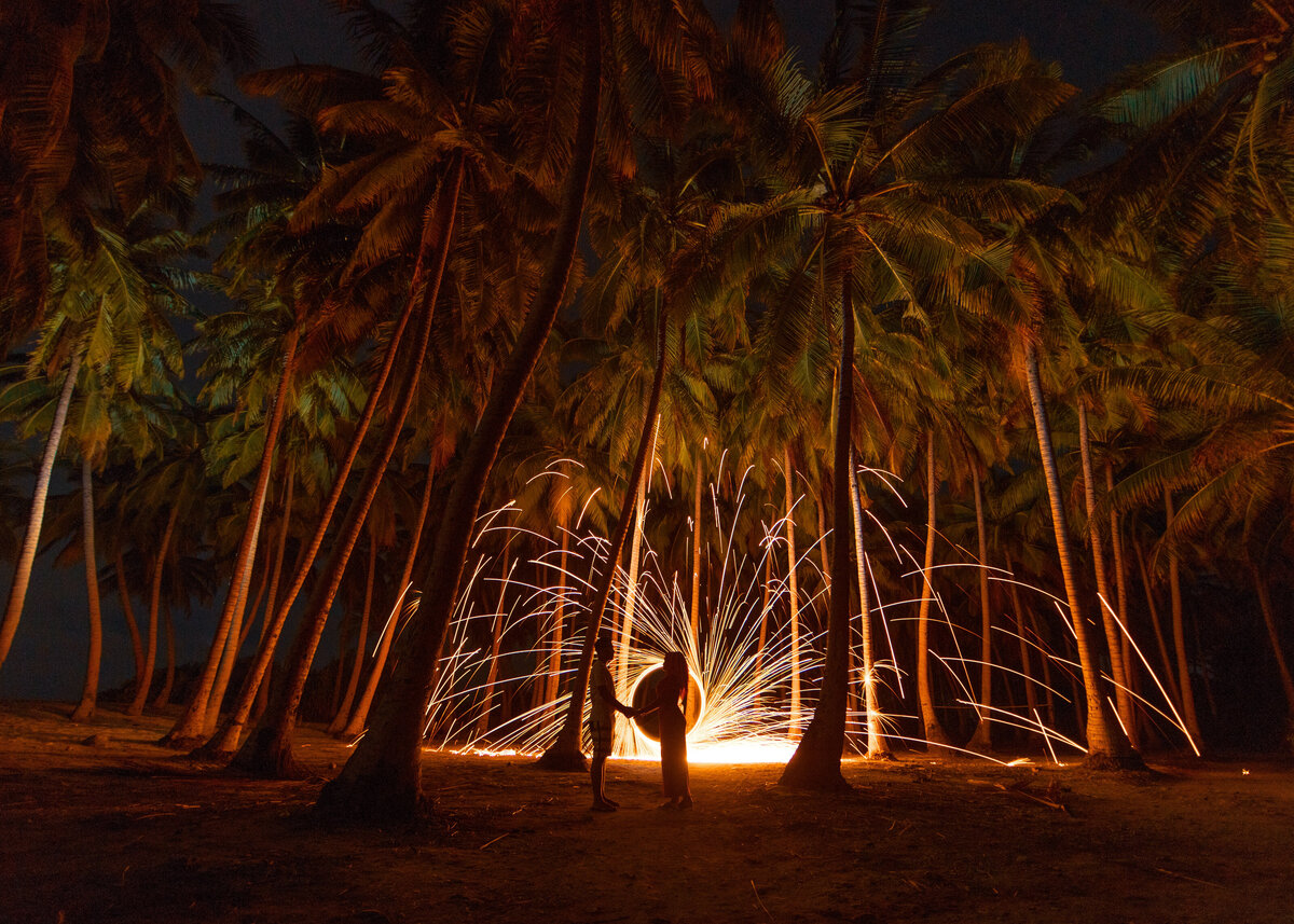 A couple are silhouetted against a catherine wheel on a beach for a wedding proposal in Barbados.