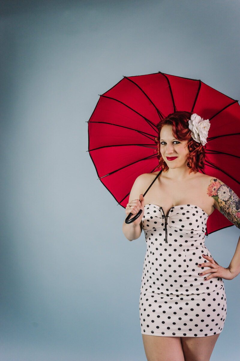 Red hair pinup girl in a white and black pinup dress and red umbrella