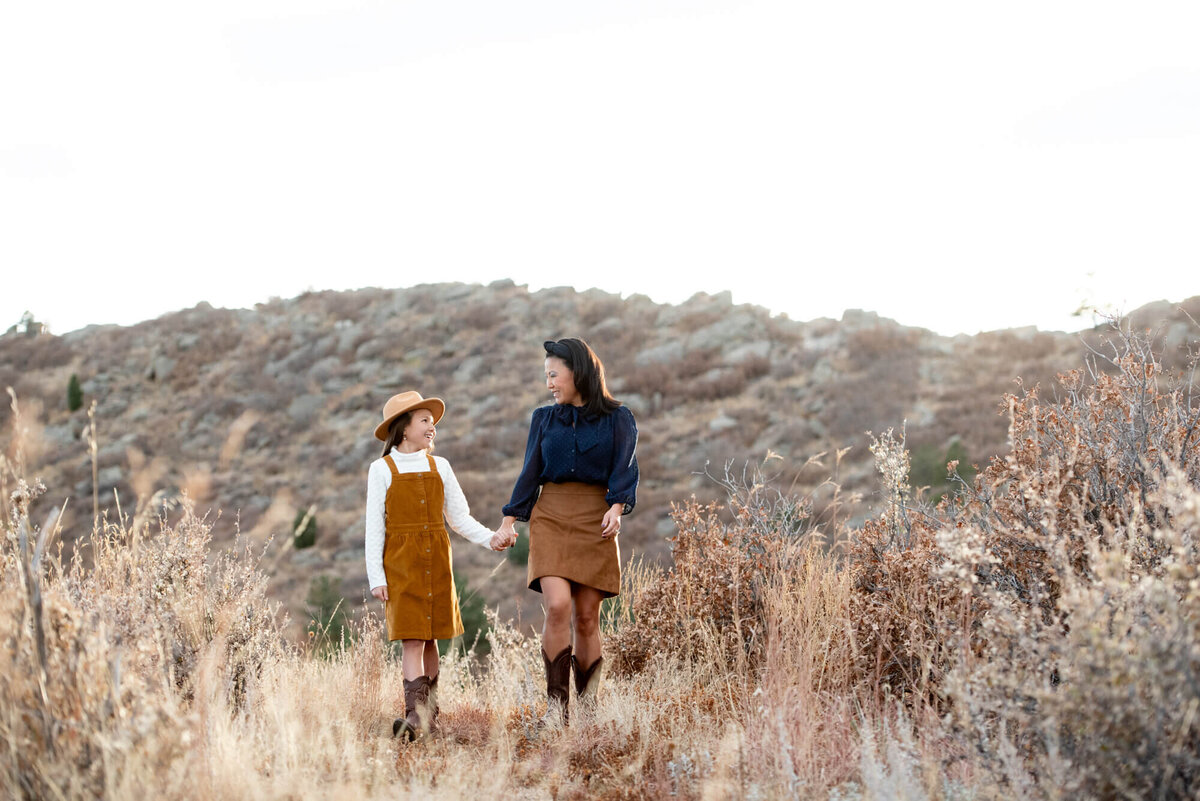 A mom and daughter hike on a trial while holding hands and laughing taken by a Colorado Springs family photographer