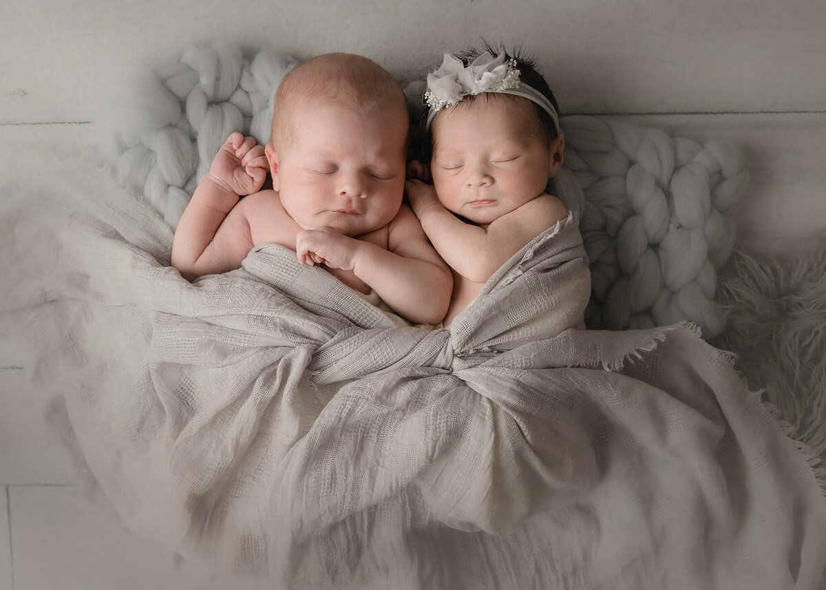 A Pella Newborn Photographer image of newborn baby twins cuddling in their sleep on a bed
