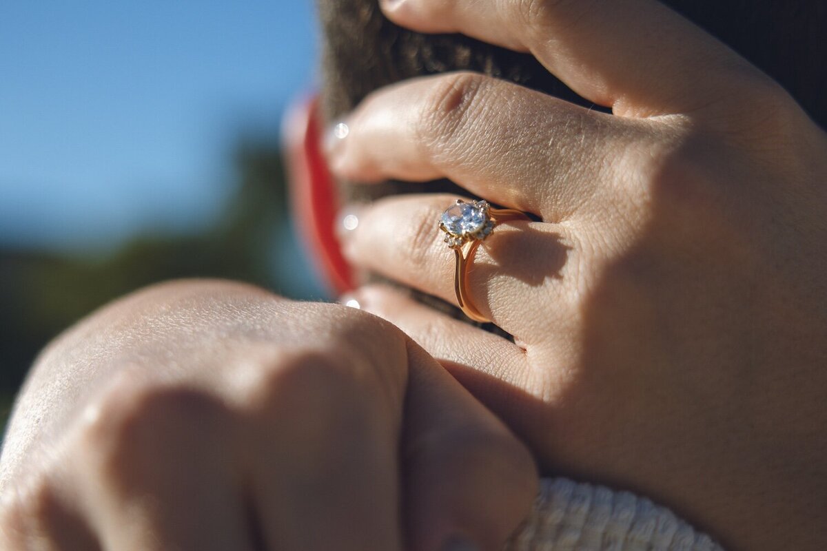 Sparkling engagement ring close-up with bride-to-be’s hand on his neck