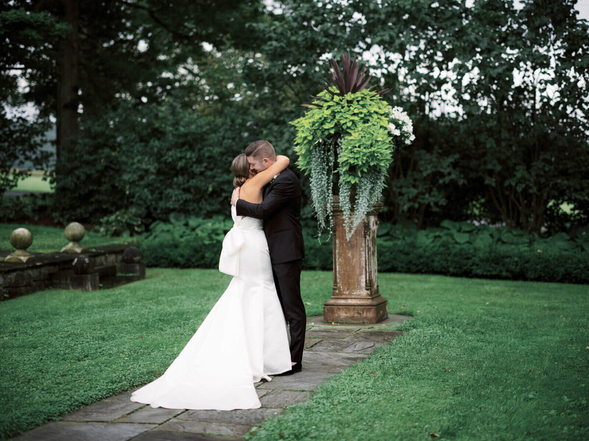 The elegant bride and groom are hugging each other in a well-manicured garden at Lion Rock Farm, CT.  Image by Jenny Fu Studio