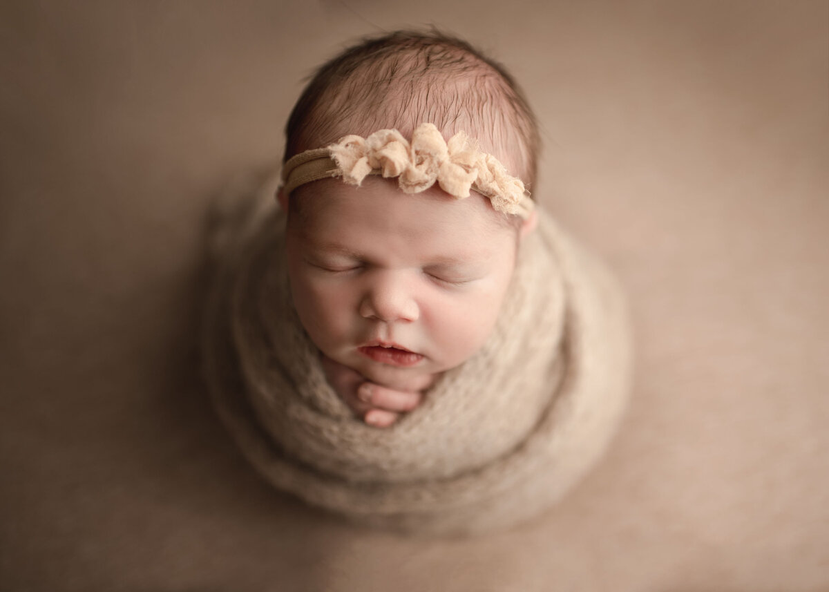 Aerial image of sleeping baby's face wrapped in beige/cream wrap and matching fabric headband