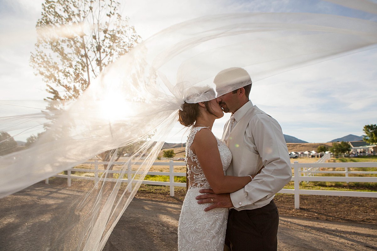 Country bride and groom kissing under long veil in the wind