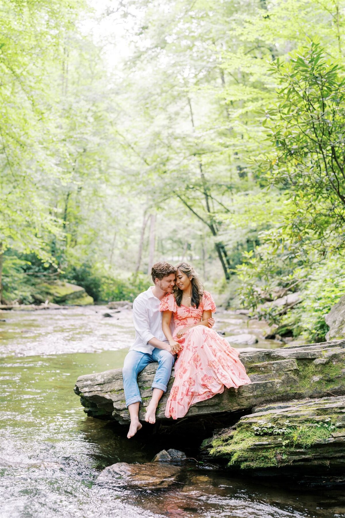 Abby and Joseph’s engagement session at Looking Glass Falls near Asheville, North Carolina, captures them sitting on a river rock in golden sunlight—like a scene from Huckleberry Finn—photographed by North Carolina wedding photographer Jessica Leigh Mason.
