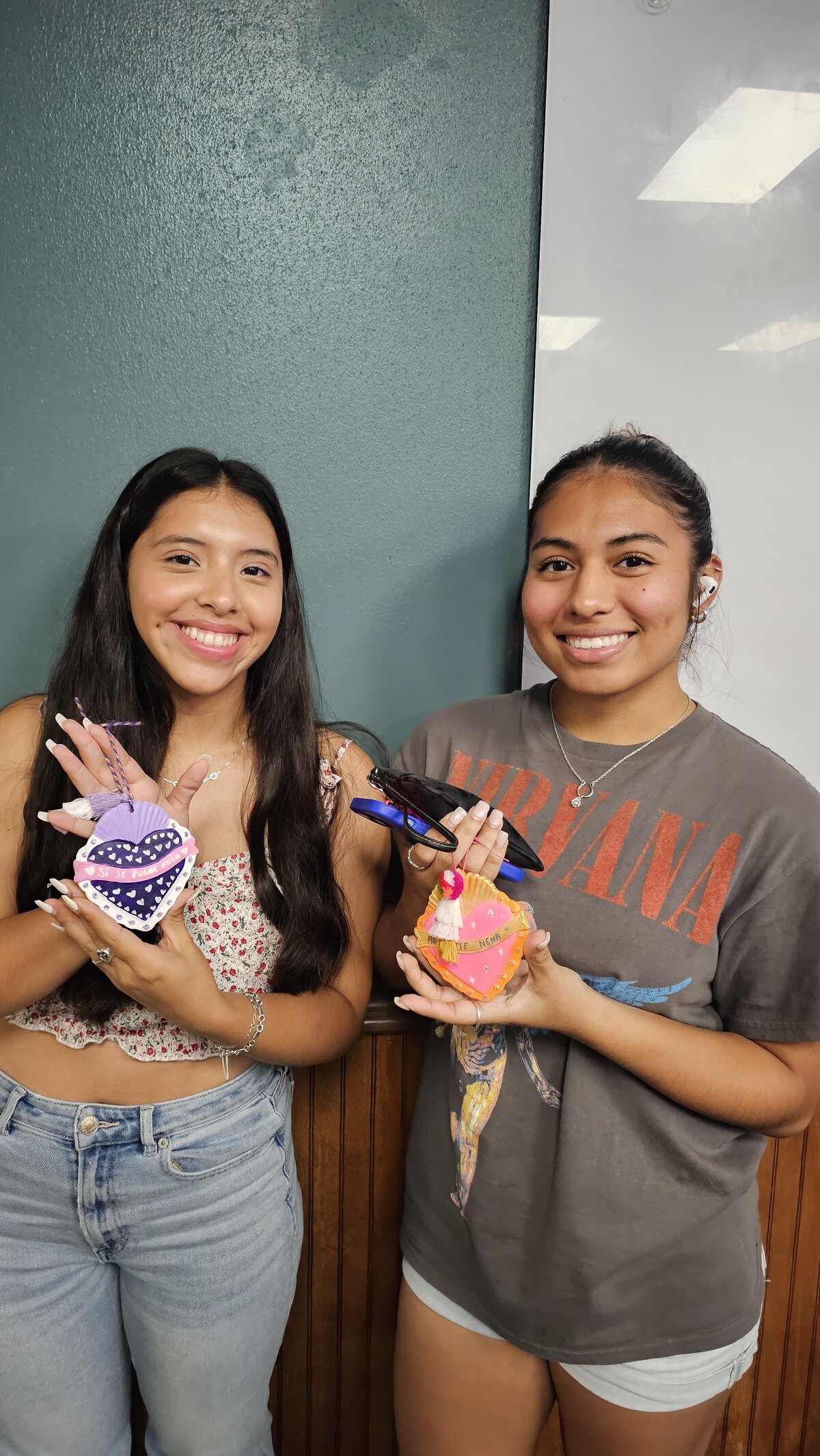 the culmination of creativity as two female students proudly display the fruits of their artistic endeavors – vibrant ceramic hearts in an array of colors.