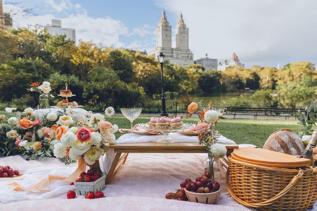 Elegant picnic spread with champagne, fruit, and florals