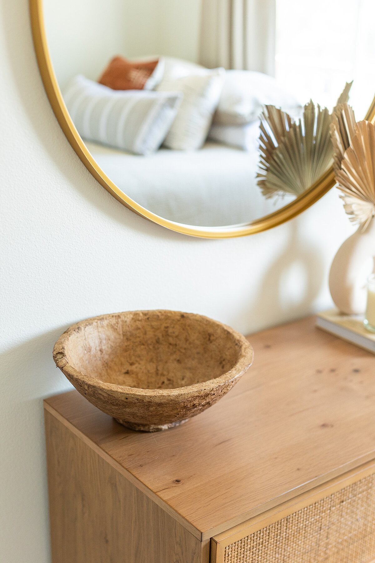 Dresser decorated with textured bowl and gold mirror in bedroom design.