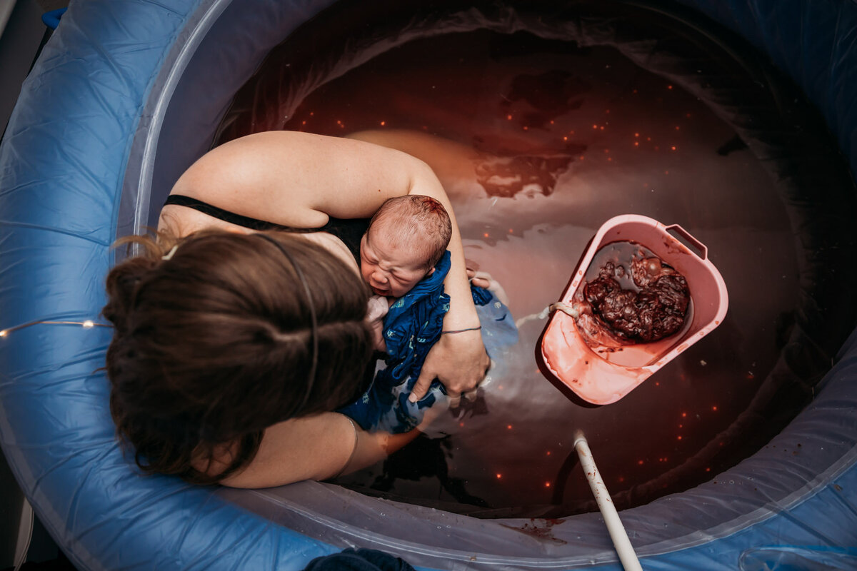 woman in birth pool holding newborn  with placenta in pool