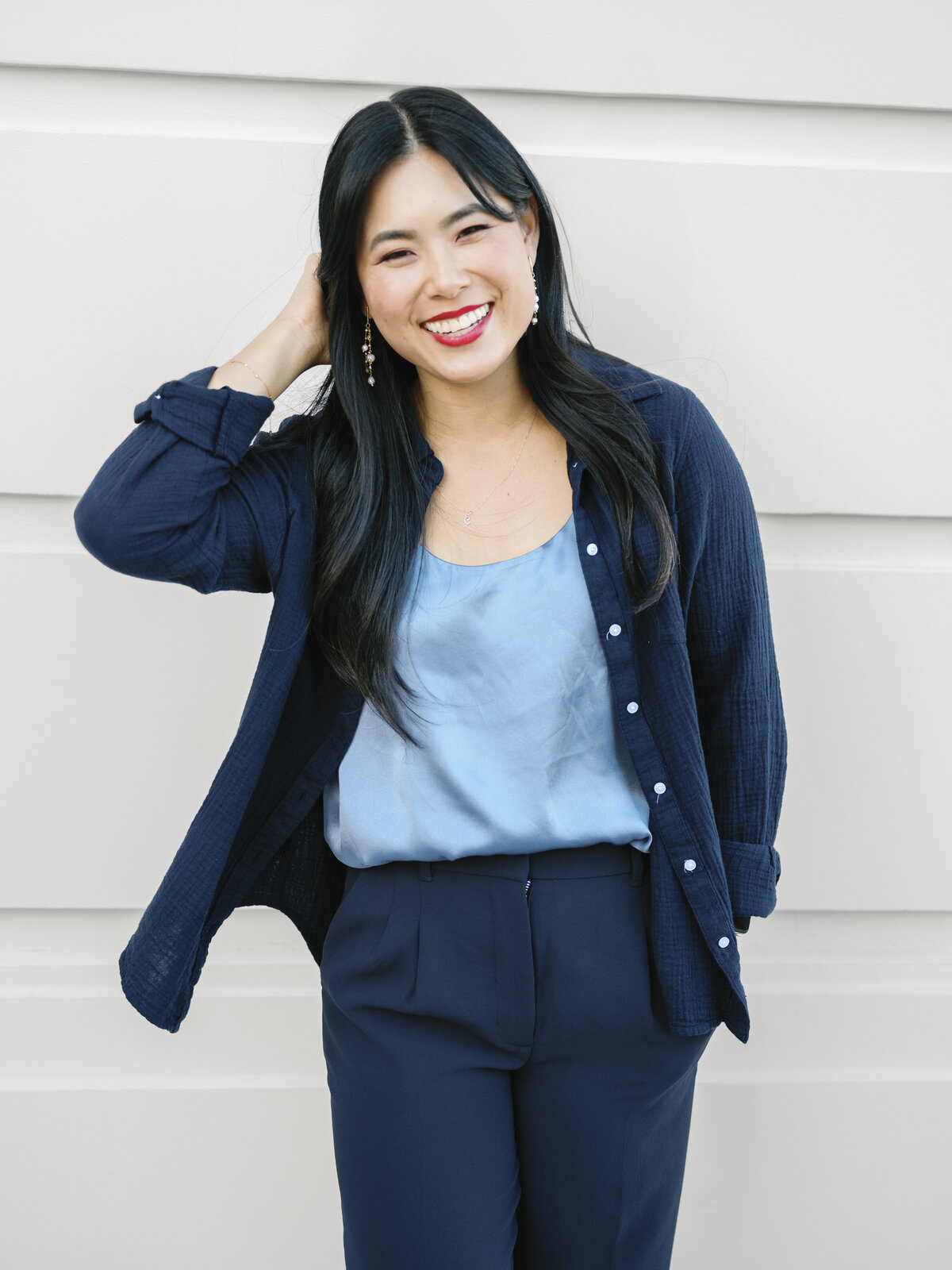 Asian woman in navy suit and light blue top posing confidently against a white wall in NYC.