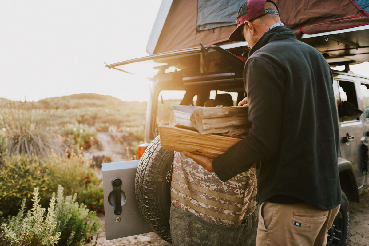 A man packing a Jeep with a rooftop tent in a scenic desert landscape, part of a luxury Southwest overland expedition from San Diego to the Grand Canyon