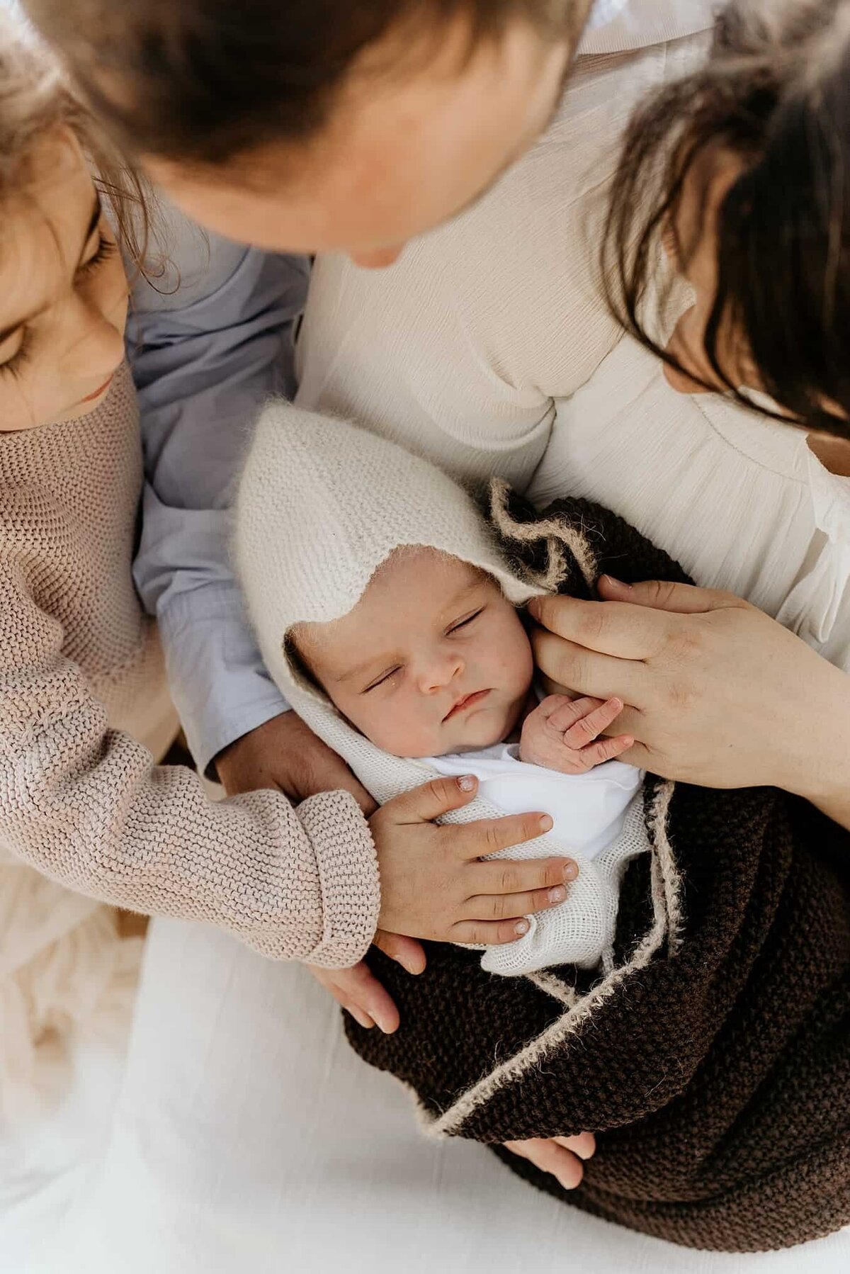Nyfødtfotografering i Oslo med baby i et teppe med foreldrene og søsken som holder rundt henne.