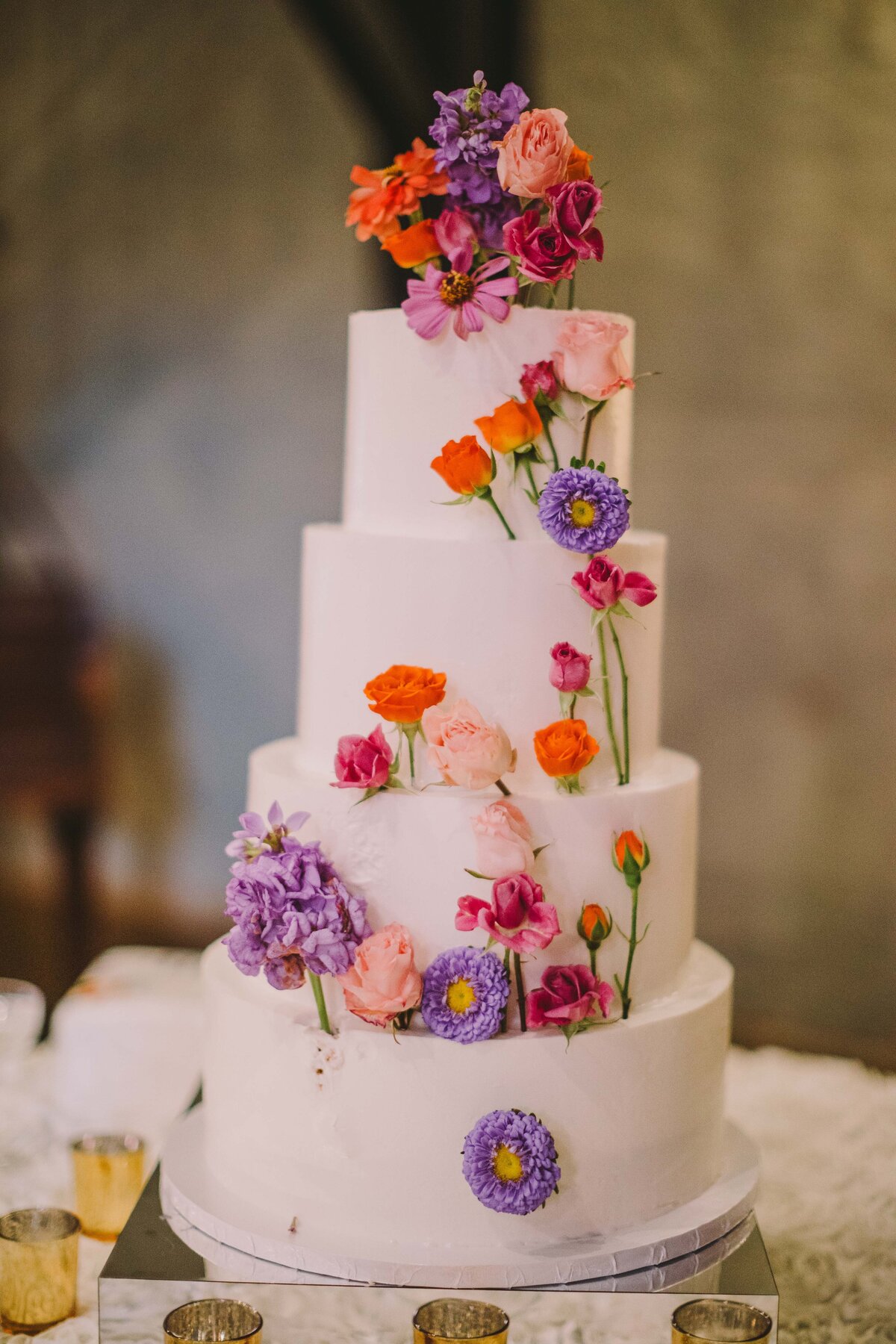 White wedding cake with purple, orange, and pink flowers.