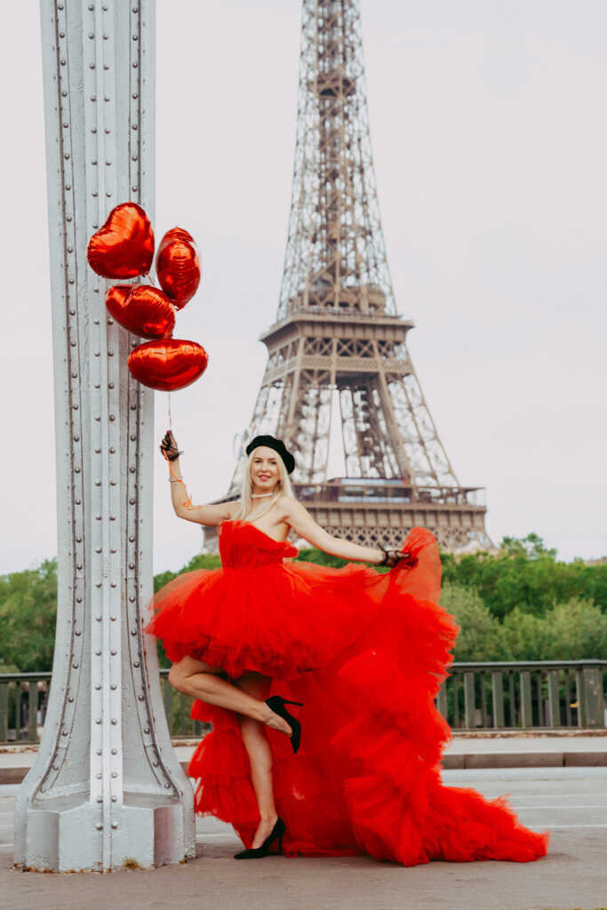 Romantic Paris photoshoot at Bir Hakeim bridge featuring woman in red dress with black beret holding heart balloons