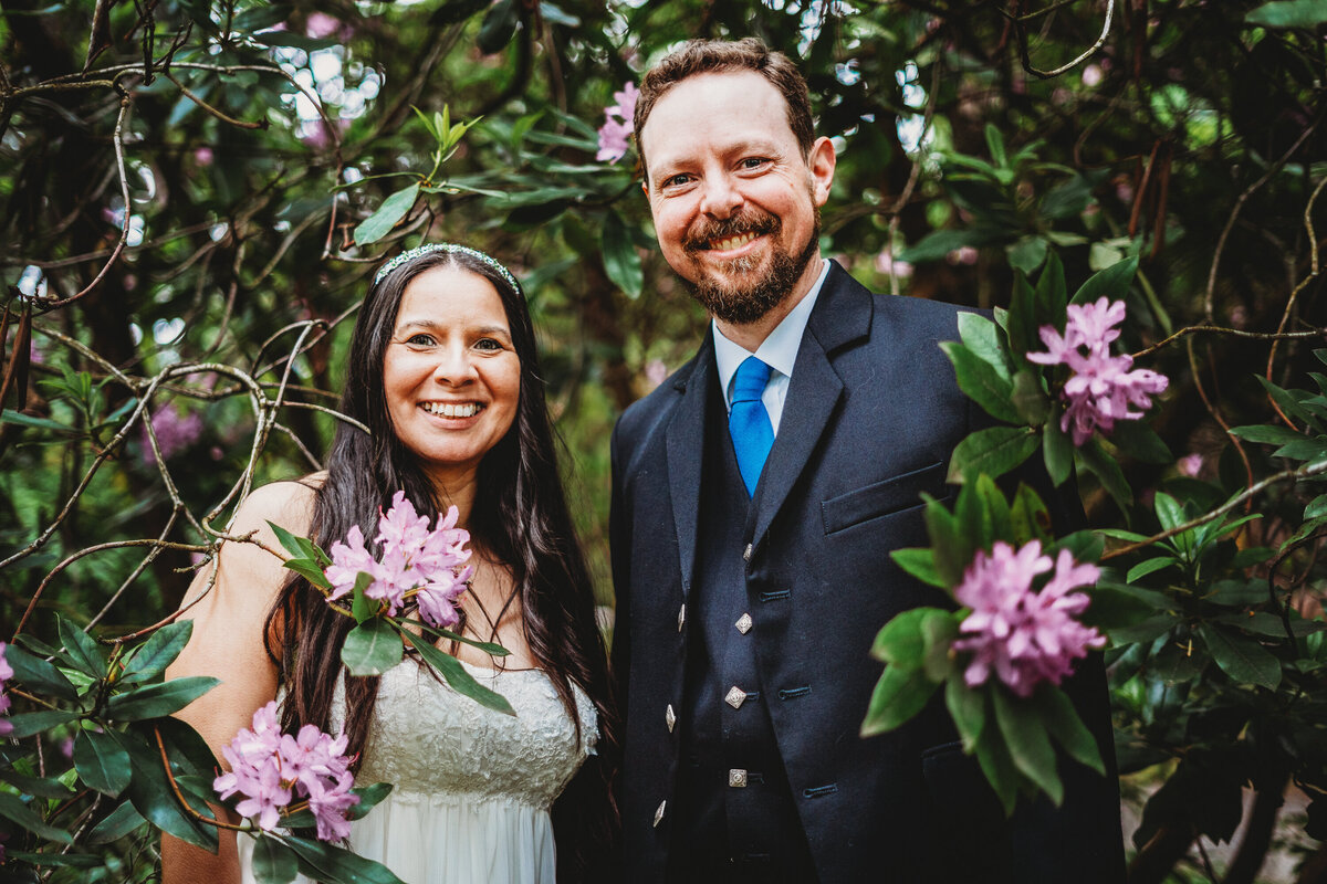 Smiling couple standing among blooming pink flowers during an outdoor portrait session in Winter Garden, Florida