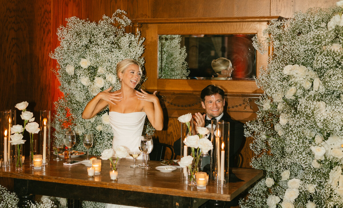 Bride and groom facing the camera holding hands while looking apart from eachother. They are standing in front of deep green trees