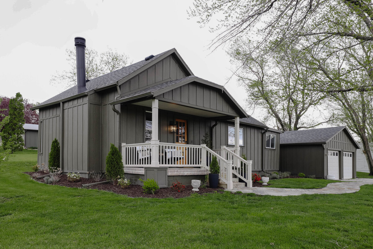 The exterior project by Nadine Stay. Board and batten siding install. Muddled Basil by Sherwin Williams exterior paint color. Flagstone path, brick front porch floor, and a custom built railing. Cabin exterior.