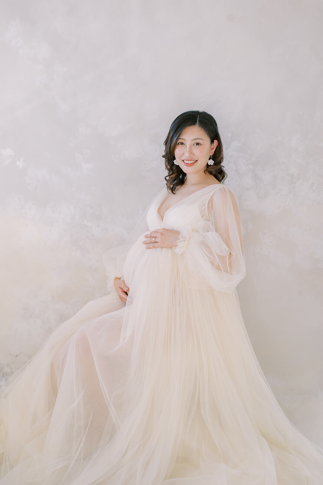 Adorned in elegance, a Chinese descent Asian mum awaits her baby's arrival in a captivating cream tulle maternity gown at a Gold Coast studio