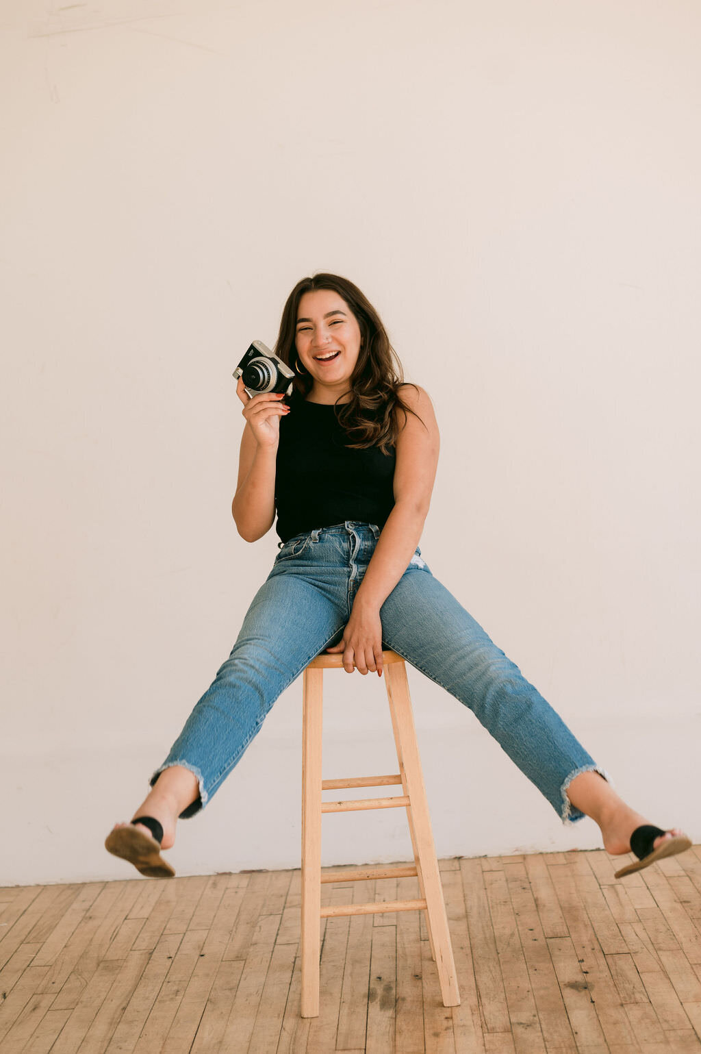 woman holding a camera with one hand and the stool she is sitting on with the other as she leans back