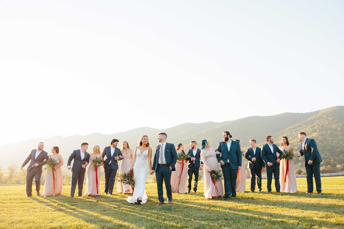 Bridal party walking with bride and groom holding hands in middle at crooked river venue during golden hour