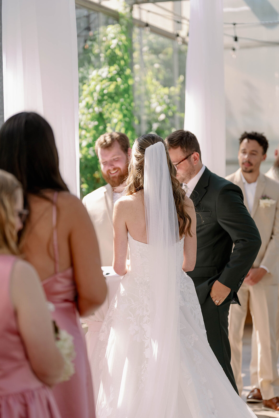 Over-the-shoulder shot of the couple from behind during their intimate Ivy House greenhouse wedding ceremony.