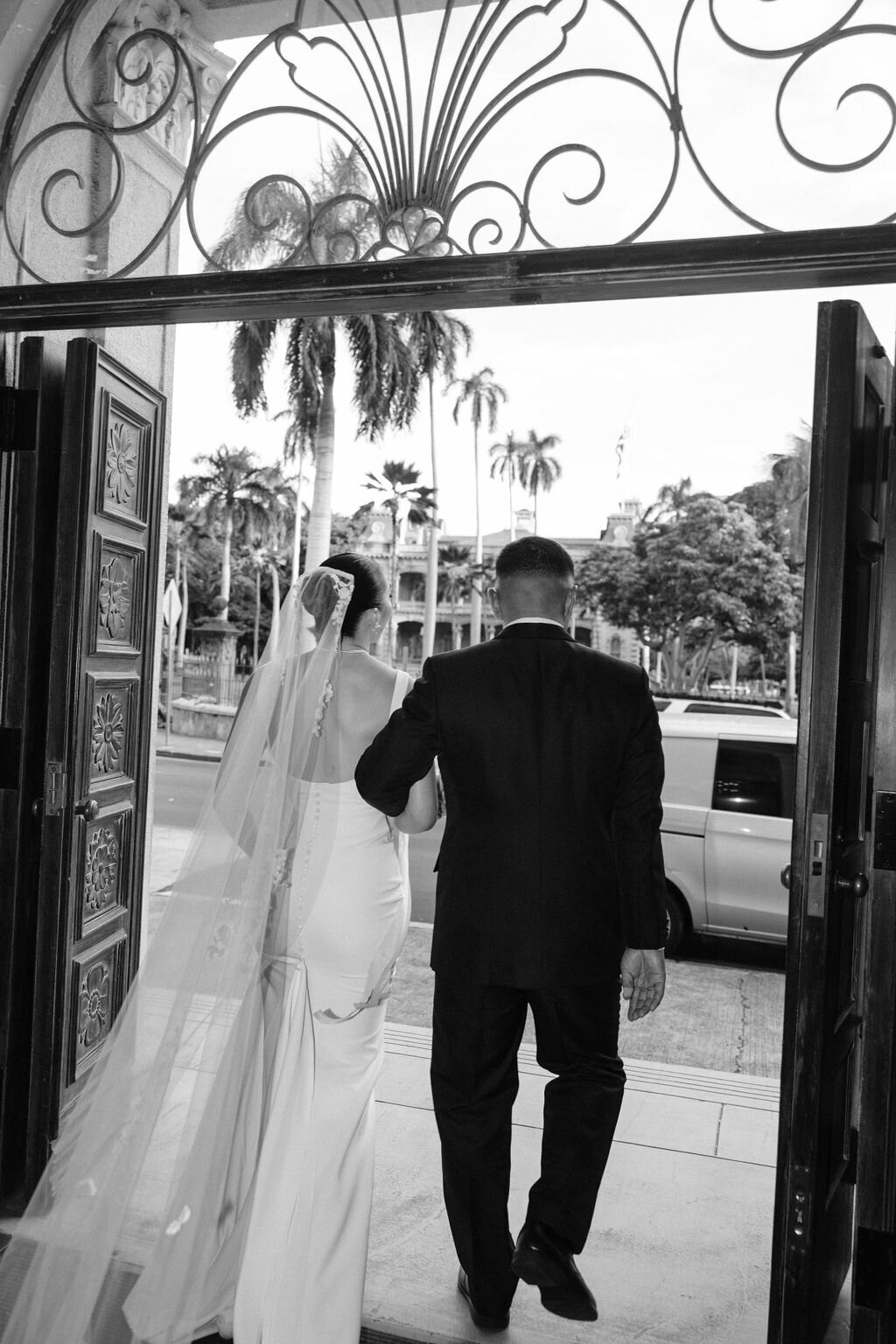 Brdie and groom walking out of wraught iron doorway towards the street